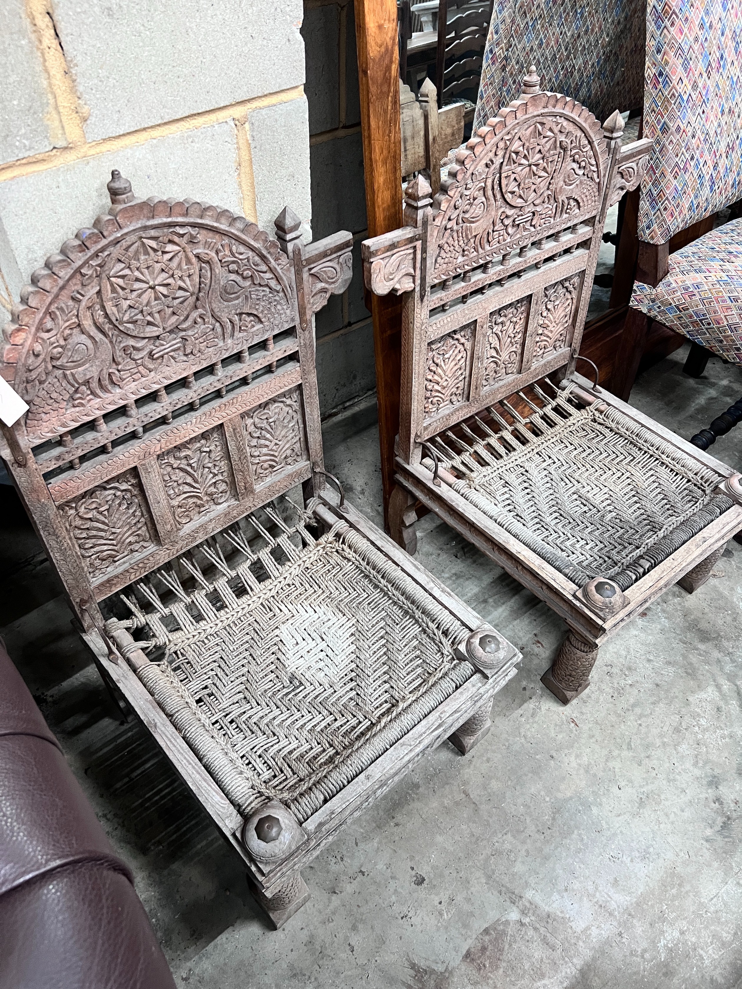 A pair of Indian carved teak low chairs with ropework seats, width 69cm *Please note the sale commences at 9am.